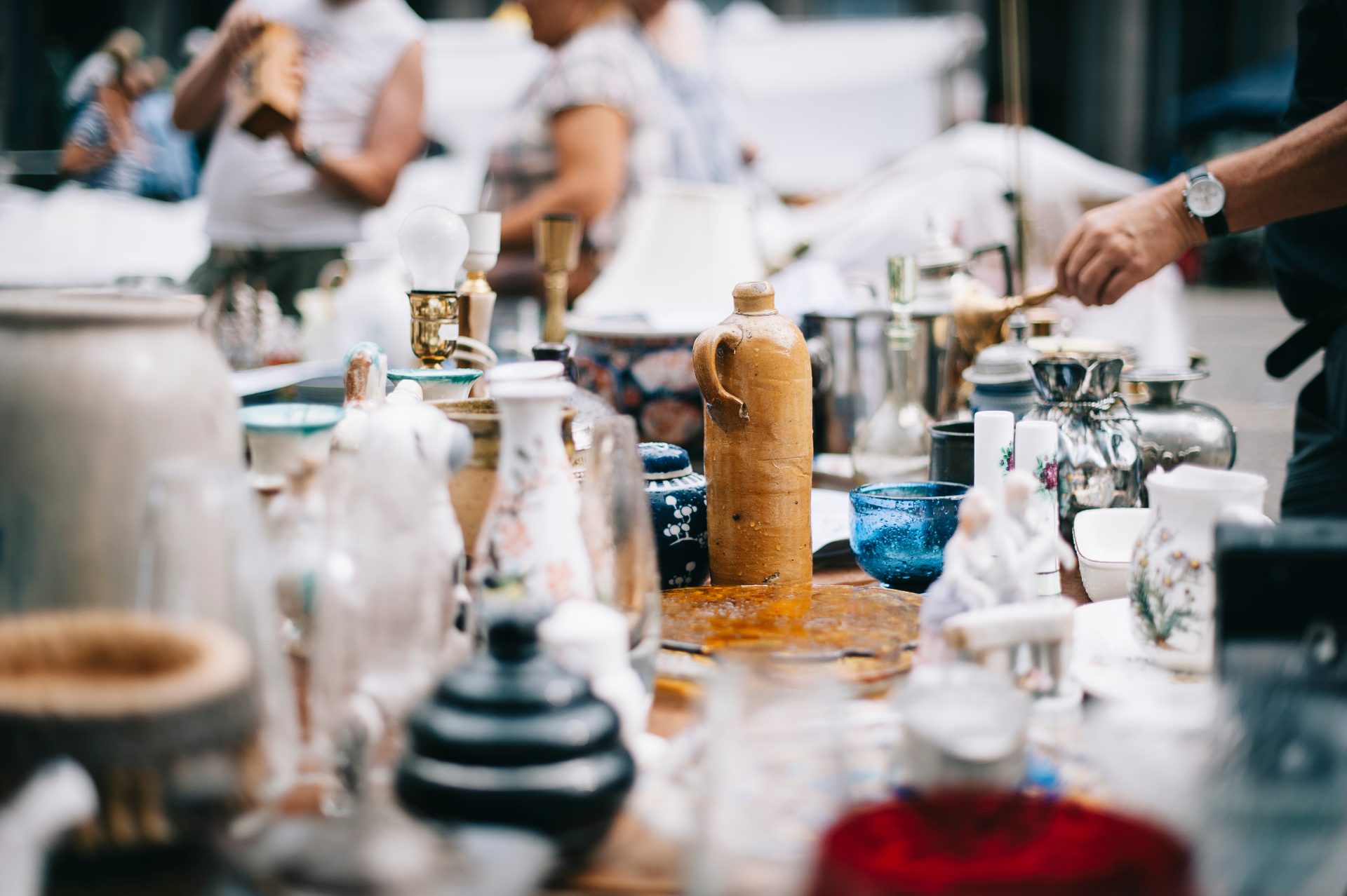 Plein d'orbets en verre, en bois et en métal reposent sur une table et des acheteurs regardent la marchandises.